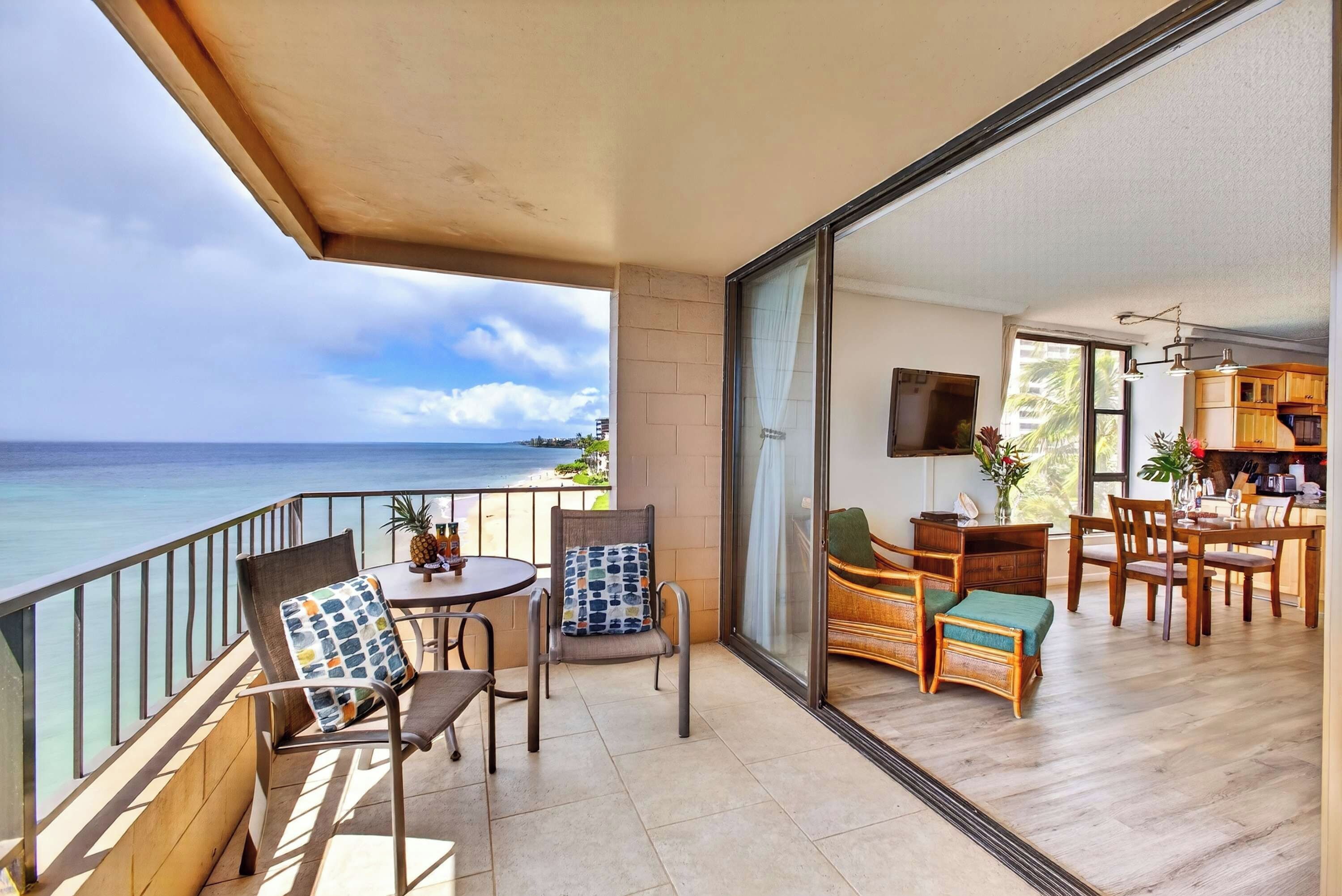 A balcony with a view of the ocean, a dining area with wooden furniture, and a kitchen with a TV.