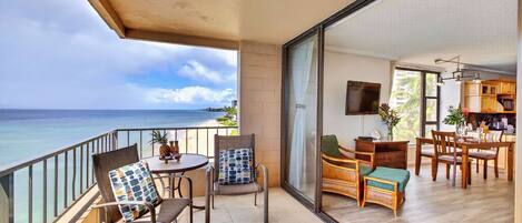 A balcony with a view of the ocean, a dining area with wooden furniture, and a kitchen with a TV.