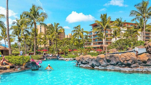 Ein Hotelpool mit Palmen, einer Felswand und einem Gebäude mit Balkonen.