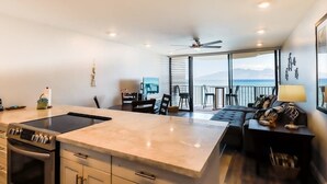 A modern kitchen with a large island, dining area with chairs, and a sofa. - *New* Fall Deal Panoramic Kahana Oceanfront for Two (Lahaina)