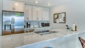 A modern kitchen with stainless steel appliances, white cabinetry, and a marble countertop. - *New* Fall Deal Panoramic Kahana Oceanfront for Two (Lahaina)
