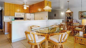 A modern kitchen with wooden cabinets, a central island with chairs, and pendant lighting. - *NEW* Fall Deal Kihei Condo for Four with Pools and Tennis by Kamaole III (Kihei)