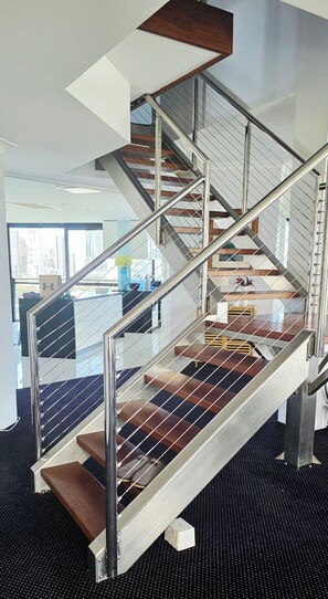 A modern staircase with metal railings and wooden steps, leading to an upper floor. - Gold Coast Penthouse Retreat - Where every window is a view! (Surfers Paradise)
