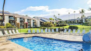 Una piscina con sillas de descanso, un área cercada y edificios modernos con paneles solares.