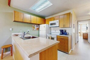 A kitchen with wooden cabinets, a microwave, a refrigerator, and a countertop. - NEW Fall $pecial Family Beach Days Across from Kamaole III in Kihei (Kihei)