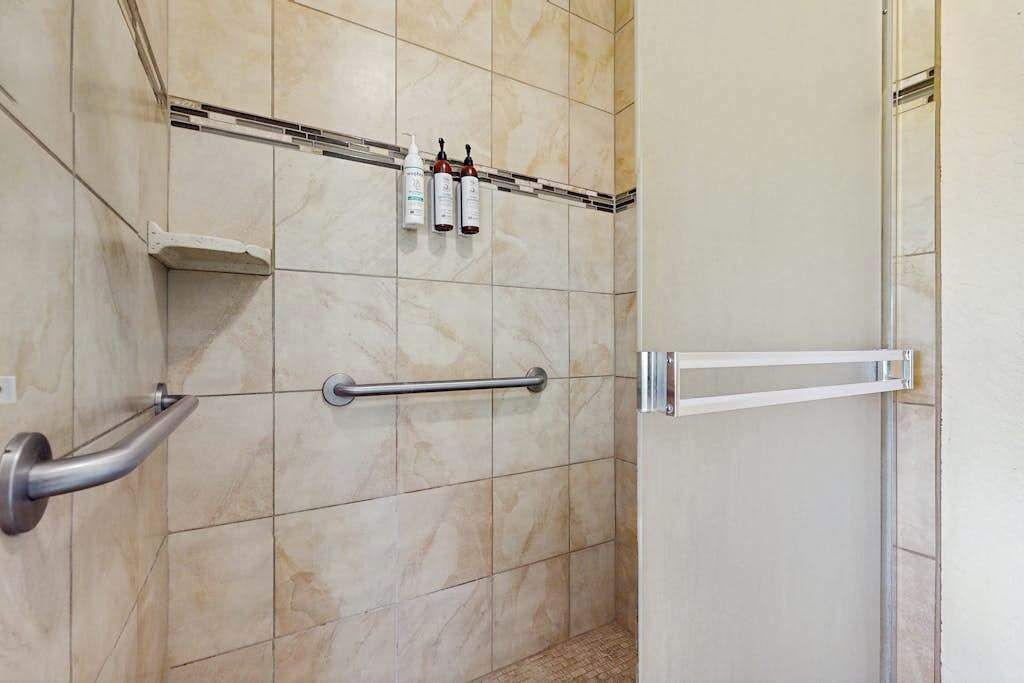 A bathroom with beige tiles, a handrail, and a door with a handle.