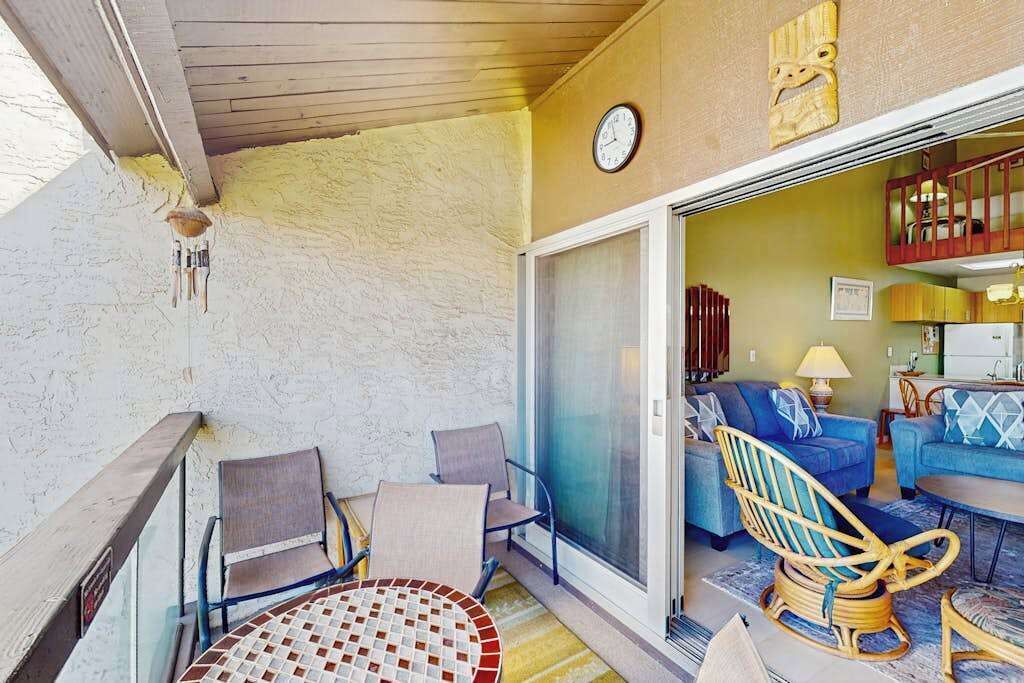 Ein Balkon mit Tisch und Stühlen, eine Glastür zum Wohnbereich mit Sofas und einem Korbstuhl.