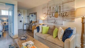 En stue med en beige sofa, et sofabord og en væg med et ananas kunstværk.