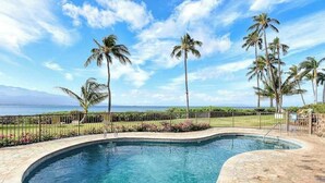 A swimming pool with a curved edge, surrounded by a stone deck, palm trees, and a view of the ocean. - *NEW* Oceanfront Ma'alaea Hideaway Near Harbor Adventures (Wailuku)