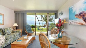 A room with a sofa, chairs, a glass table, a lamp, a painting of a sea turtle, and a view of the ocean. - *NEW* Oceanfront Ma'alaea Hideaway Near Harbor Adventures (Wailuku)