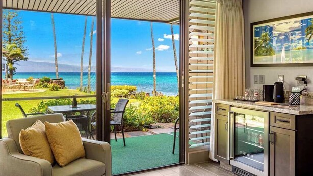 Ein Zimmer mit einer Schiebeglasdoor zum Balkon mit Blick aufs Meer und Palmen.
