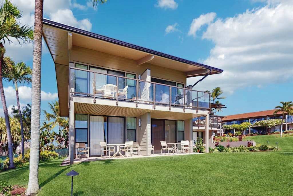 Un hotel moderno de dos pisos con balcón, mobiliario exterior y césped cuidado.