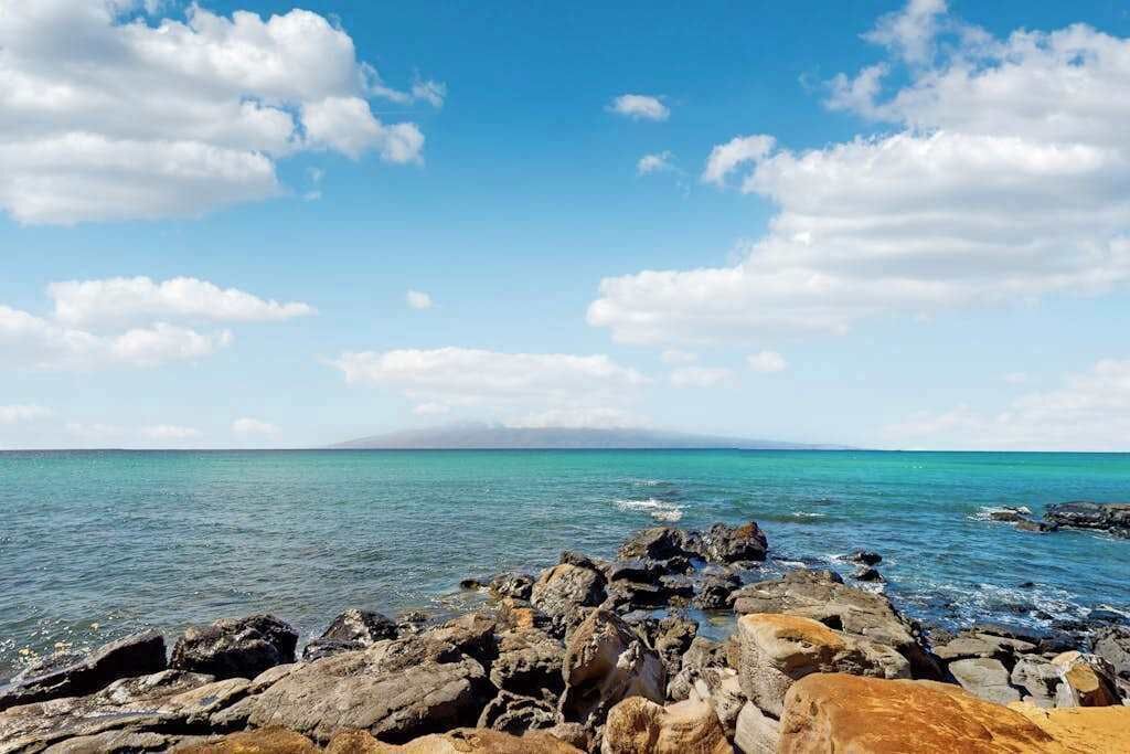 Una costa rocosa con agua turquesa cristalina y una montaña a lo lejos.