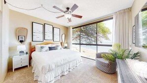 Quarto com cama, ventilador de teto, janela com vista e mesa de cabeceira com abajur.