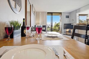 Een eettafel gedekt voor twee personen, met wijnglazen en een fles wijn, een uitzicht op de natuur en een televisie op de achtergrond.