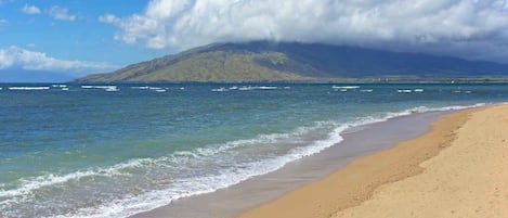 A beach with a mountain in the background, clear skies, and calm sea.