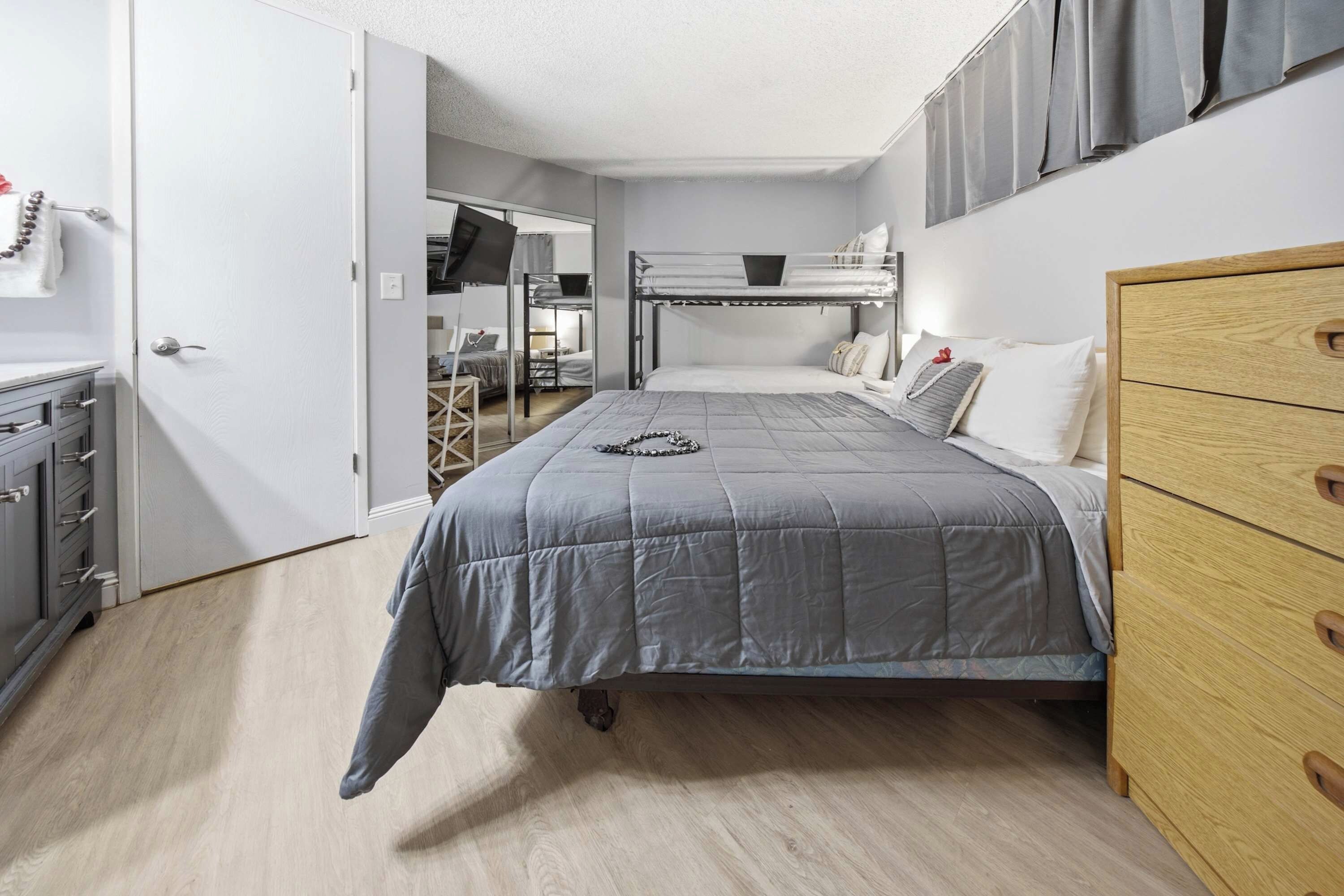 A compact bedroom with a bunk bed, a wooden dresser, and a desk with a chair.