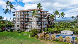 A multi-story hotel with balconies, a swimming pool, and a view of the ocean. - New Oceanfront Kihei Condo with Pool and Hot Tub (Kihei)