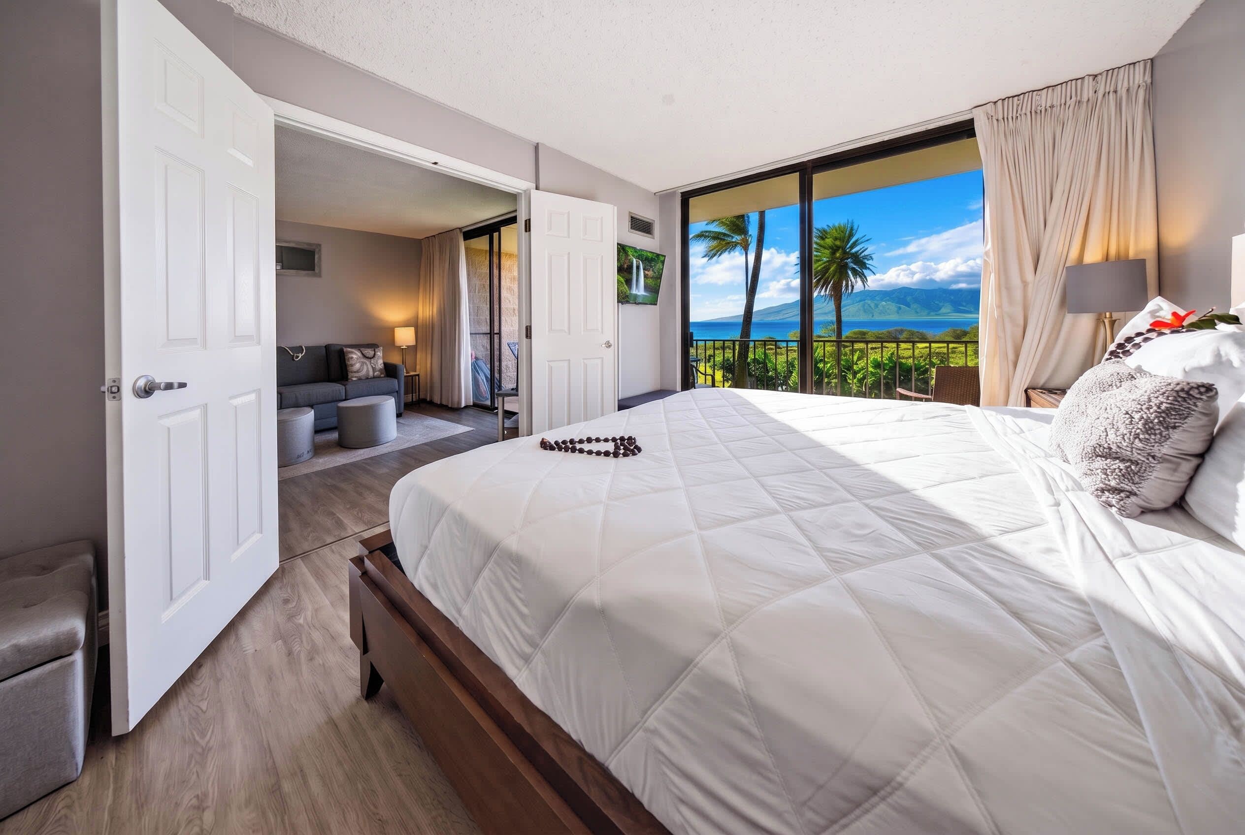 Quarto de hotel com uma cama grande, varanda com vista para o mar e área de estar separada com vista para o quarto.