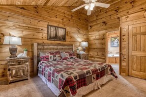 Ein Schlafzimmer in einer Holzhütte mit einem Bett, zwei Nachttischen, einem Deckenventilator und einer Tür.