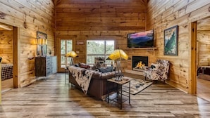 Ein Holzblockhaus-Interieur mit Kamin, einer Couch, einem Fernseher und einem Essbereich.