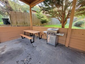 Eine Außenpatio mit Grill, zwei Holzbanken und einem überdachten Bereich.