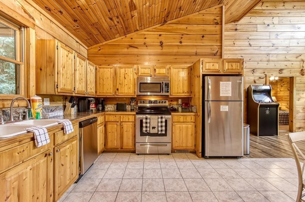 Ein Interieur einer Holzhütte mit einer Küche, die Holzschränke, eine Mikrowelle, einen Herd und einen Kühlschrank beinhaltet.