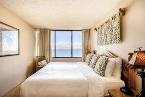 Een hotelkamer met een groot bed, uitzicht op zee, een schilderij aan de muur en een lamp op het nachtkastje.