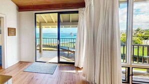 Ein Zimmer mit Holzboden, einer Schiebetür zum Balkon mit Meerblick und einem kleinen Teppich.