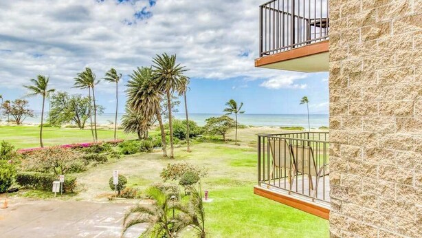 Hotel met balkon, uitzicht op een grasveld met palmbomen en het strand.
