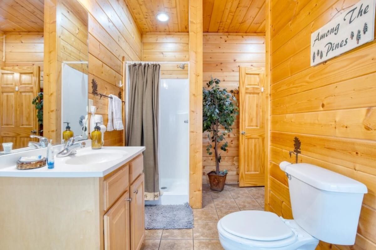 A wooden cabin bathroom with a sink, toilet, shower, and a sign on the wall.