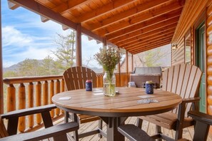 Eine Holzterrasse mit einem runden Tisch, Stühlen, einer Blumenvase und einem Grill.