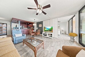 A spacious living area with a ceiling fan, a television, and a dining area with wooden furniture. - *New* Fall Deal Oceanfront Kahana Stay, Walk to Pohaku Park (Lahaina)