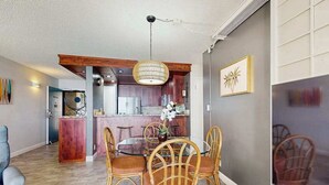Un comedor con sillas de mimbre y una mesa de vidrio, una cocina con armarios de madera y una lámpara colgante.