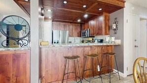 Una cocina con gabinetes de madera, un refrigerador de acero inoxidable, un microondas y una zona con taburetes de bar.