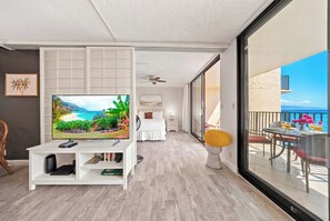A modern living room with a flat-screen TV, a white entertainment unit, and a balcony with a table and chairs. - *New* Fall Deal Oceanfront Kahana Stay, Walk to Pohaku Park (Lahaina)
