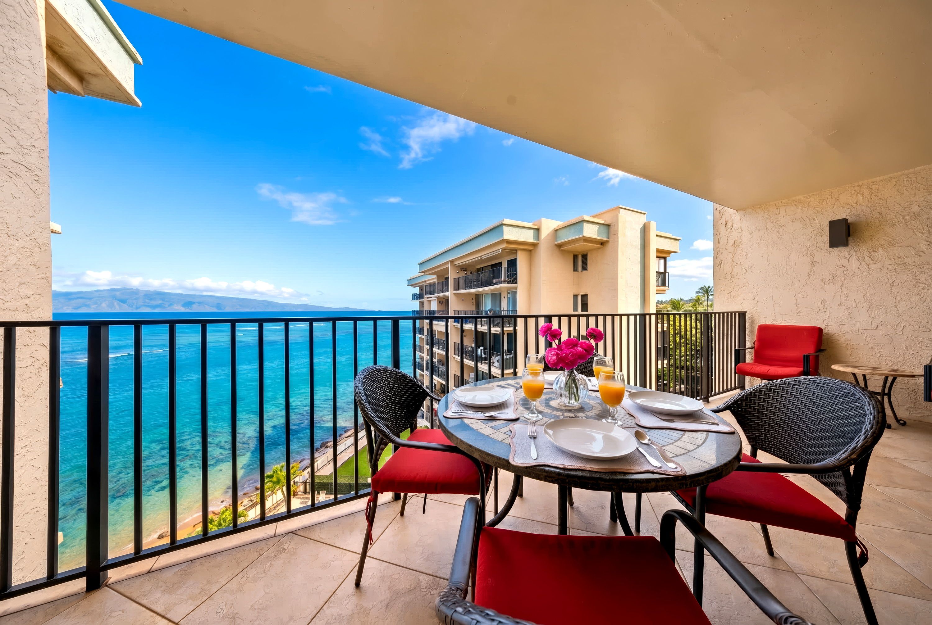 A balcony with a table set for two, overlooking a beach and a building.