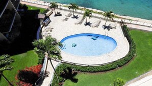 Una piscina circular con un deck perimetral, palmeras y vistas al océano.