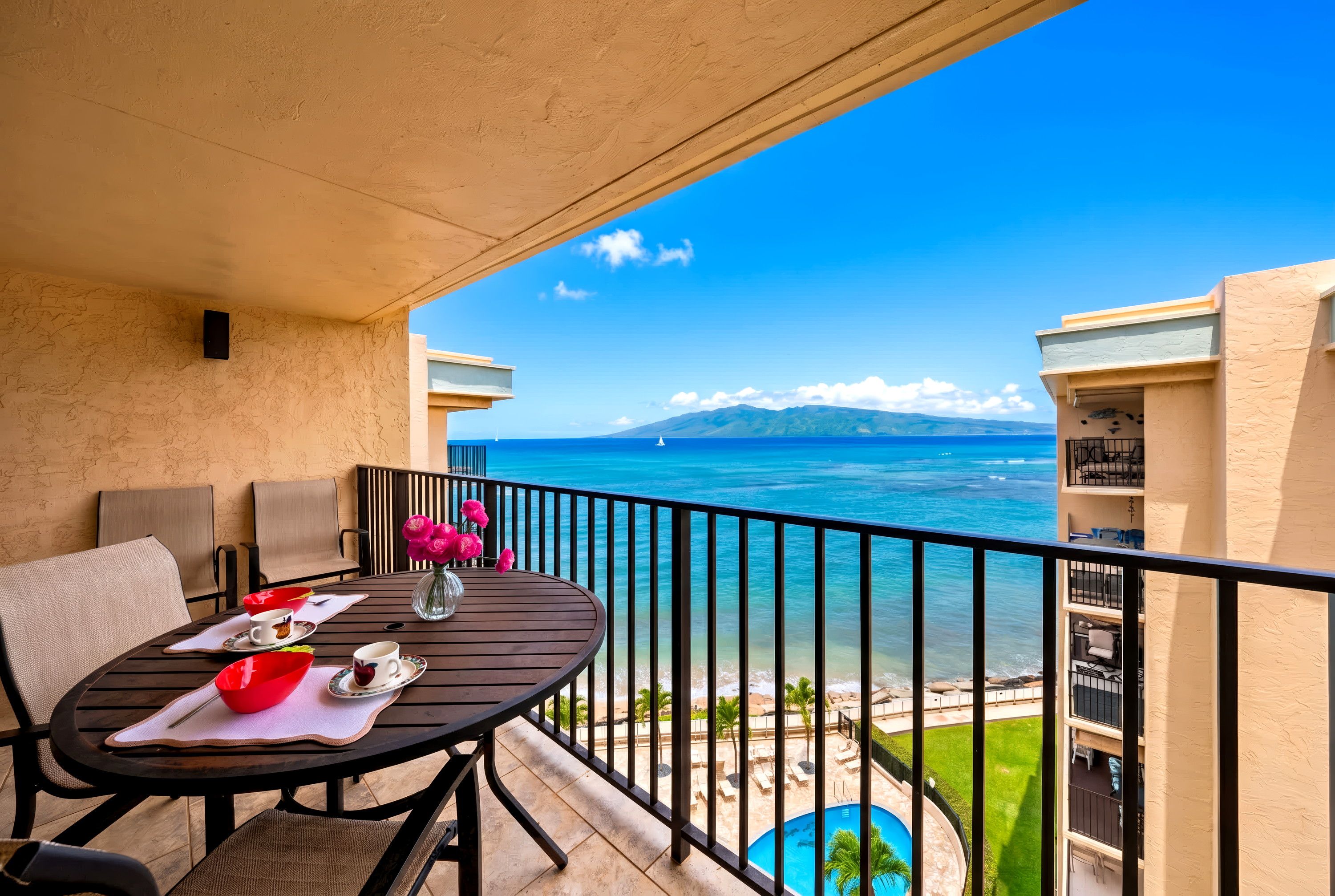 Ein Balkon mit einem Tisch für zwei Personen, mit Blick auf einen Pool und einen Strand.