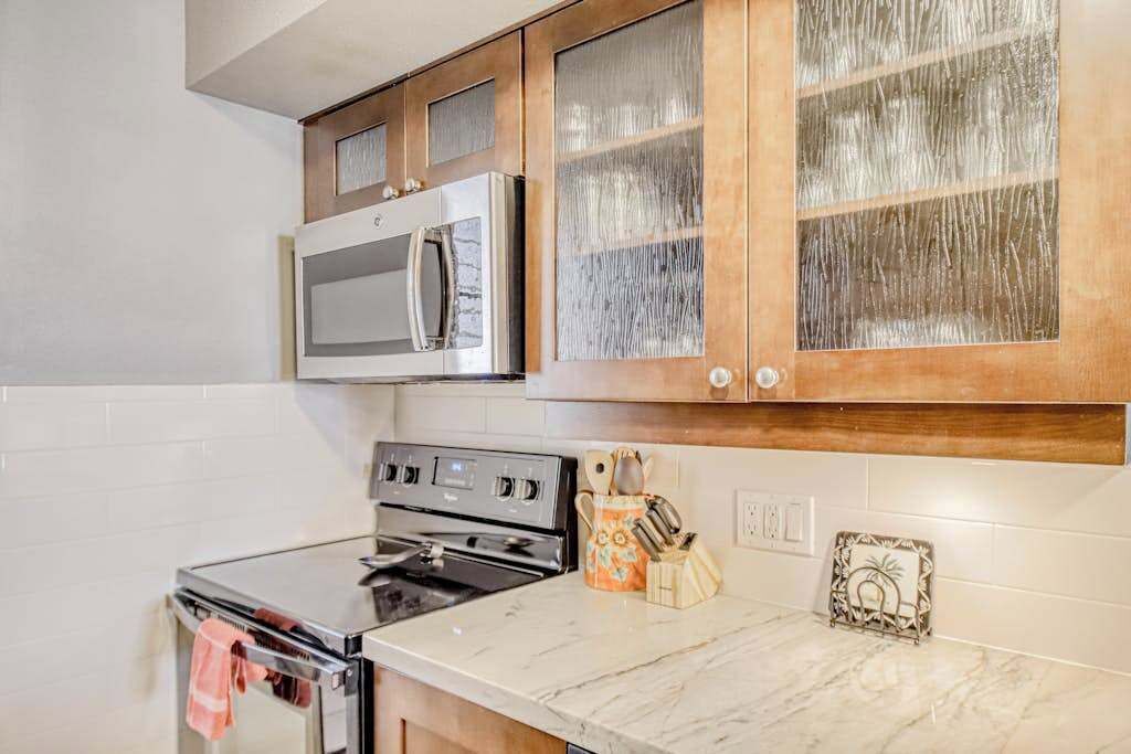 A kitchen with a stainless steel oven, a microwave, wooden cabinets, and a marble countertop.