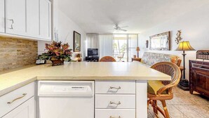 A kitchen with white cabinets, a dishwasher, a dining area with wicker chairs, and a ceiling fan. - New Kihei Ocean-View Retreat for Two with Beachfront Pool (Kihei)