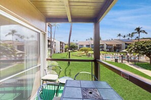 A balcony with a table and chairs, overlooking a pool and a well-maintained lawn with palm trees. - *New* Fall Special Garden-View Kihei Base for Four Near Kamaole III Beach (Kihei)