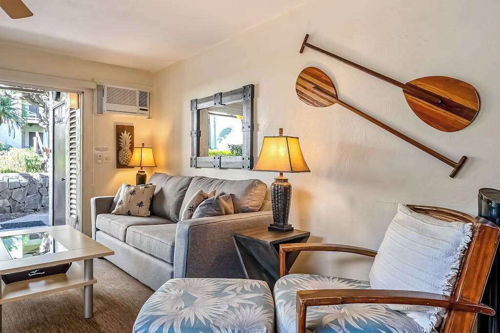 A living room with a sofa, a coffee table, a chair, a lamp, a mirror, and two wooden paddles on the wall.