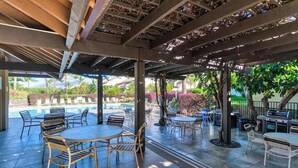 An outdoor patio area with tables and chairs, a grill, and a pool in the background. - NEW Fall Sale Garden-View Kihei 1BR with Pools and Tennis (Kihei)