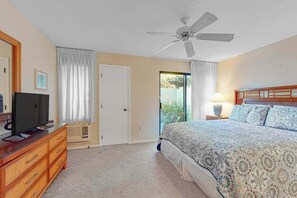 A bedroom with a bed, a TV, a dresser, a ceiling fan, and a door leading to a balcony. - NEW Fall Sale Garden-View Kihei 1BR with Pools and Tennis (Kihei)