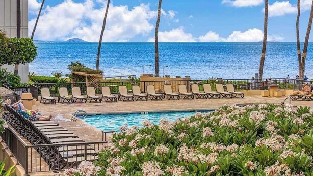 A poolside area with lounge chairs, a pool, and a view of the ocean. - New Beachfront Couple’s Base at Sugar Beach (Kihei)
