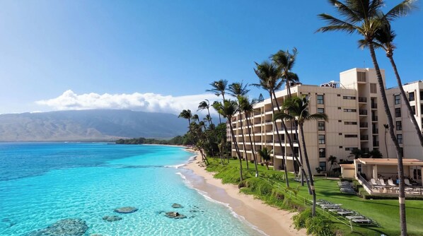 A beachfront hotel with a clear view of the ocean, palm trees, and a mountainous backdrop. - New Beachfront Couple’s Base at Sugar Beach (Kihei)