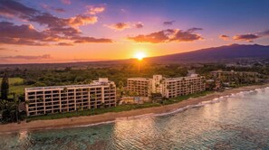 Un hôtel situé en bord de mer, composé de plusieurs bâtiments, avec une plage et une vue sur le coucher de soleil.