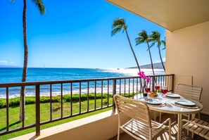 Un balcon avec une table dressée pour deux personnes, donnant sur une plage bordée de palmiers et sur l’océan.