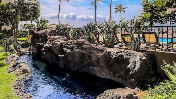 A pool area with a rocky water feature, palm trees, and lounge chairs. - NEW Fall Deal Ocean-View Sugar Beach Escape for Two (Kihei)
